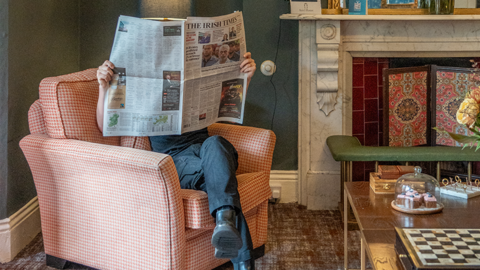 Guest relaxing in armchair reading newspaper in Ariel House drawing room
